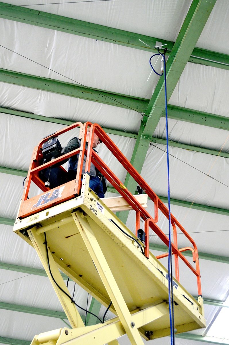 Yellow and red scissor lift raised close to the steel roof trusses of an industrial building